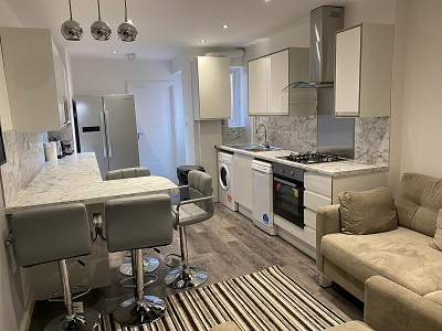 Open-plan kitchen with breakfast bar stools, white cabinets, and beige sofa
