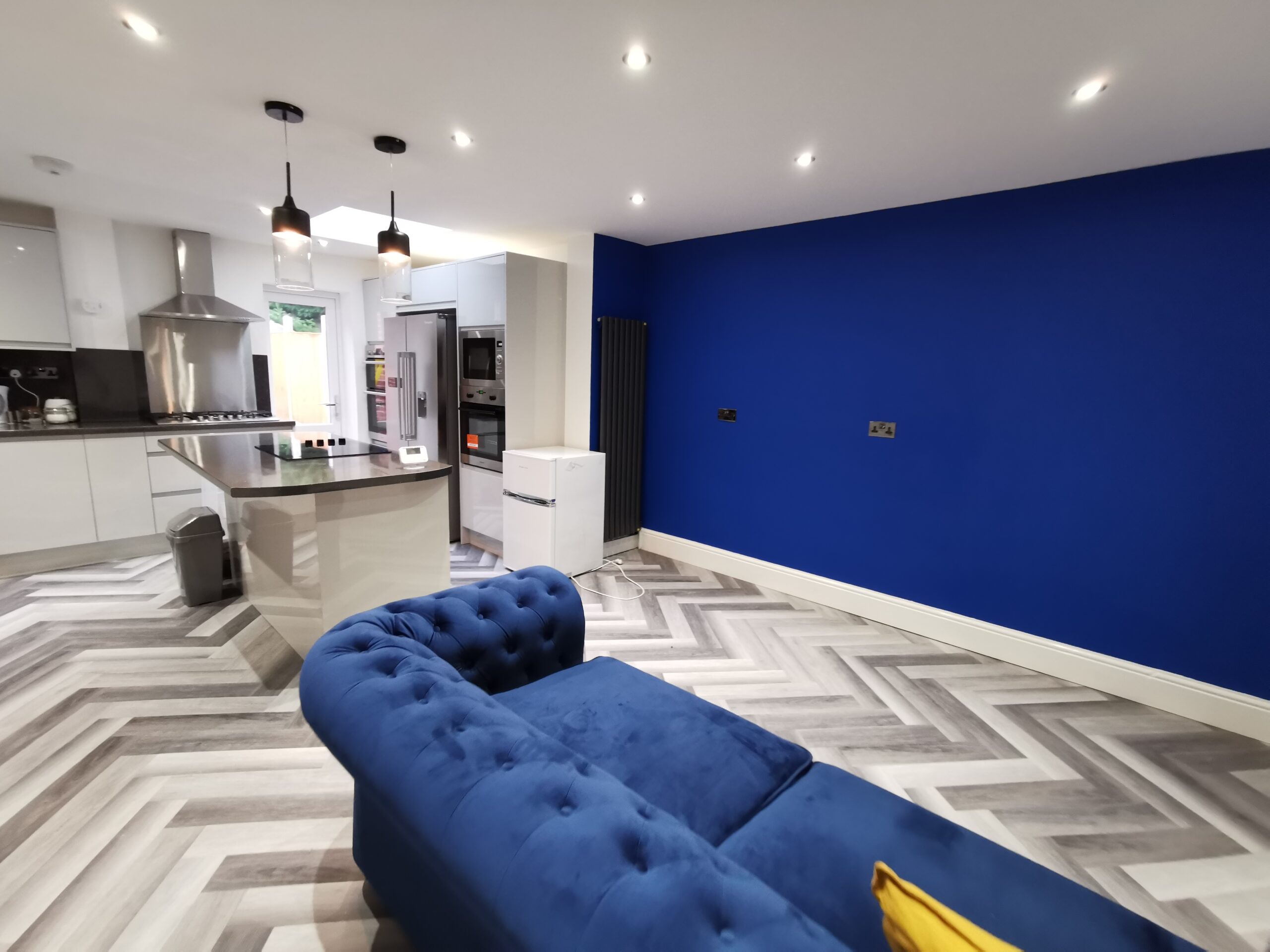 Open-plan kitchen and living room with blue feature wall and velvet sofa
