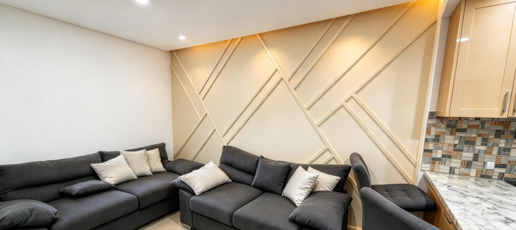 Living room with geometric cream panelled wall, grey sofas, and kitchen corner